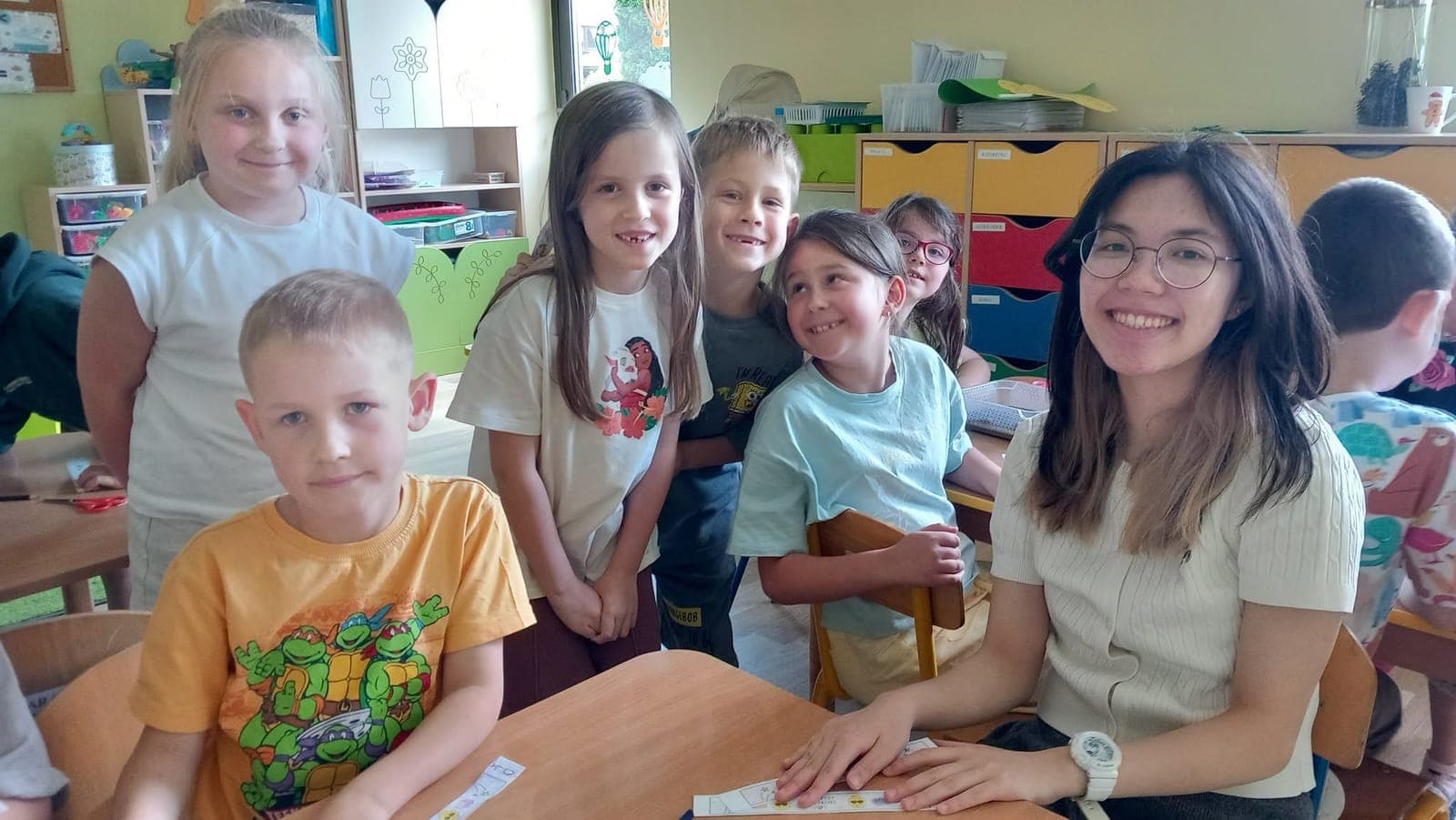 Children and an exchange participant smiling at a table in a bright classroom
