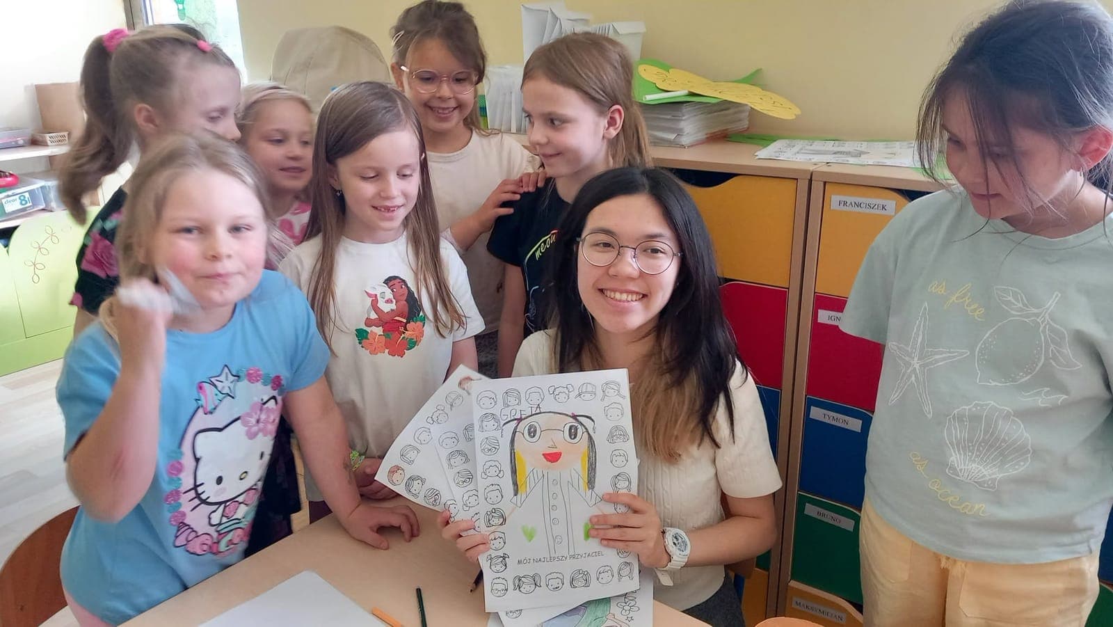Children proudly showing colouring pages next to an exchange participant