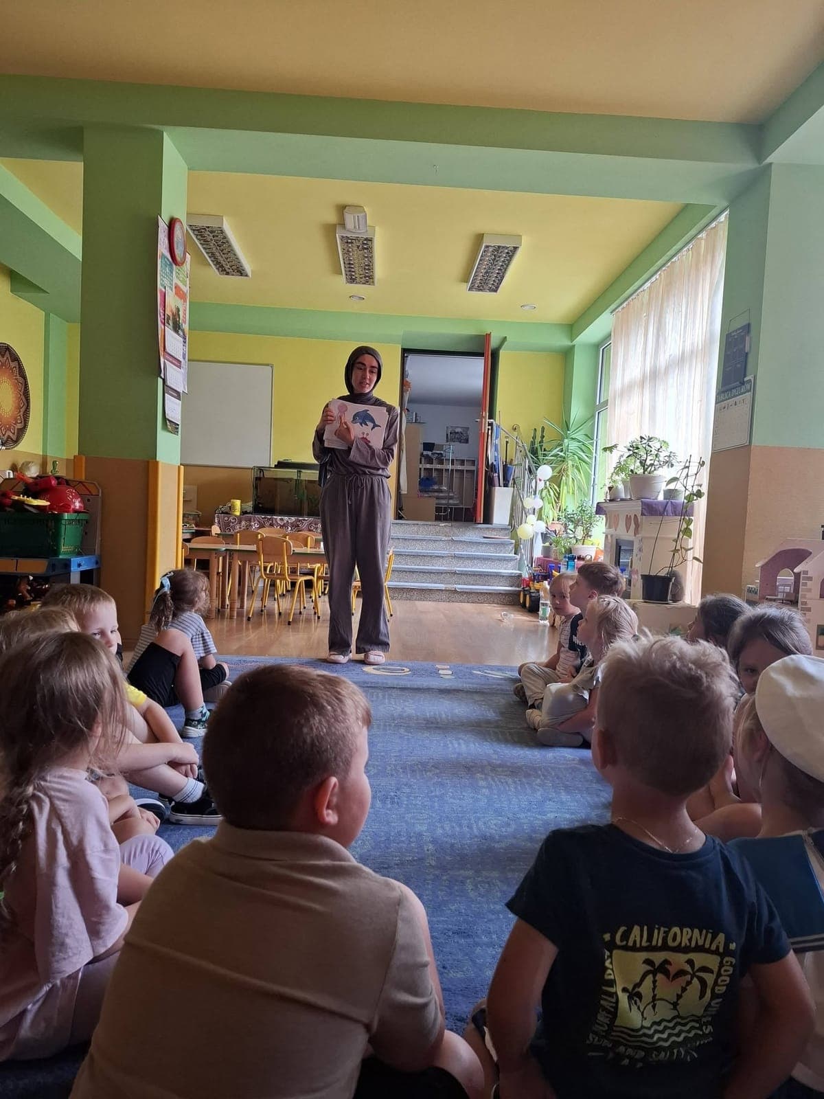 An exchange participant reading to children sitting on a carpet in a school hall