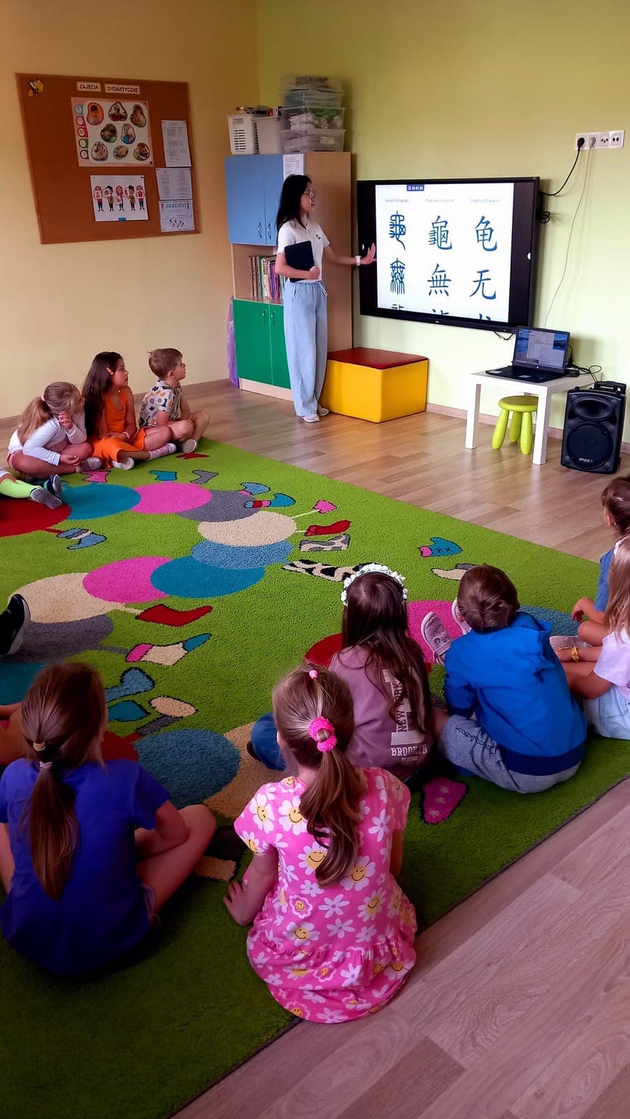 An exchange participant teaching children sitting on a classroom carpet